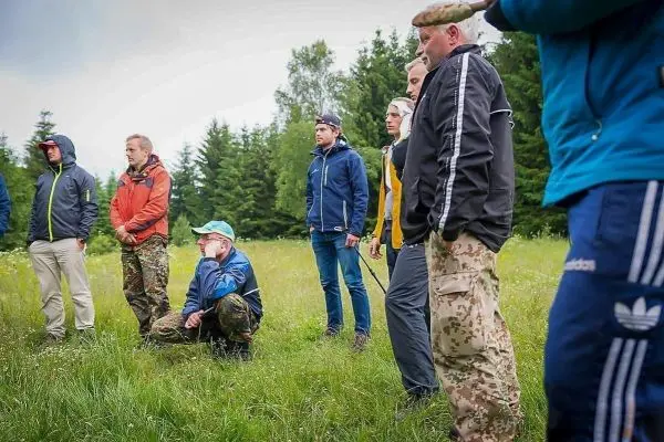 Gruppe von Personen in Outdoor-Bekleidung steht auf einer Wiese umgeben von Bäumen