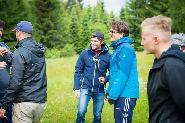 Gruppe von Personen in Outdoor-Bekleidung steht auf einer Wiese und unterhält sich