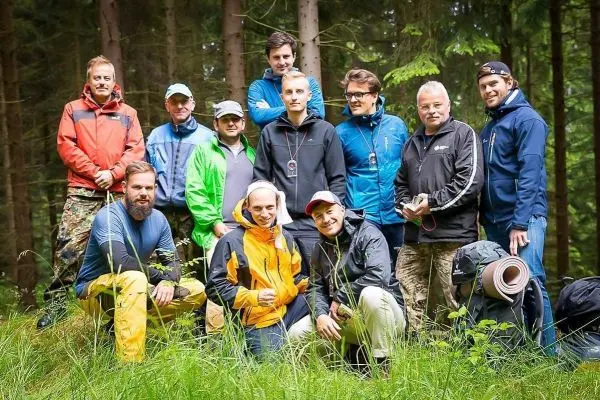Gruppe von Personen in Outdoor-Bekleidung steht im Wald auf Grasfläche
