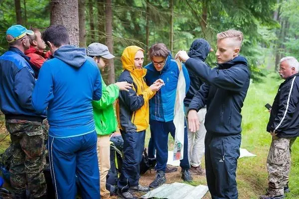 Gruppe von Personen in Outdoor-Bekleidung steht im Wald und interagiert miteinander