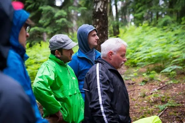 Gruppe von Personen in Regenjacken steht im Wald zwischen Bäumen und Farnen