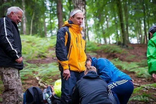 Gruppierung von Personen in einem Wald, eine Person erhält Erste Hilfe