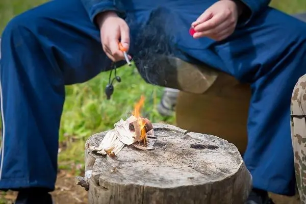 Kleine Flamme brennt auf einem Holzstück, während eine Hand Zunder hält