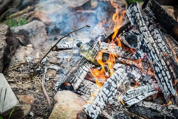 Kleine Flamme brennt zwischen verkohltem Holz und einer Flasche