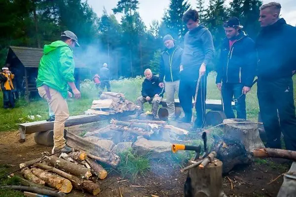 Kleines Bodenfeuer mit Rauch, umgeben von Holzscheiten und mehreren Personen