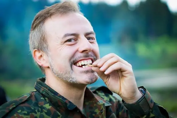 Lächelnder Mann in Tarnkleidung hält etwas zwischen den Zähnen