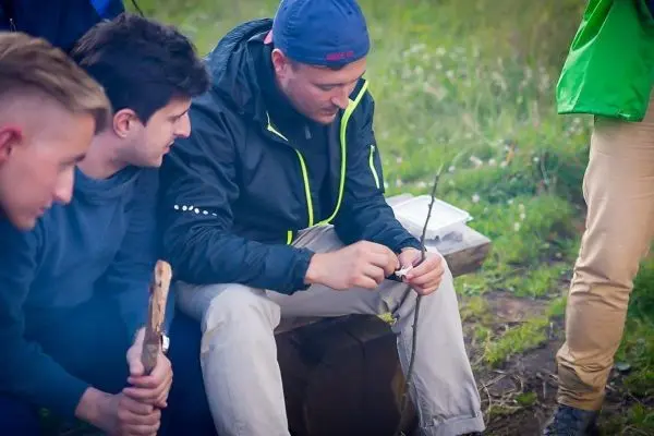 Mann bearbeitet einen Stock mit einem Messer, während andere zuschauen