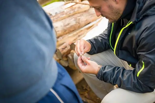 Mann bearbeitet Zunder mit einem Messer, Holzstapel im Hintergrund