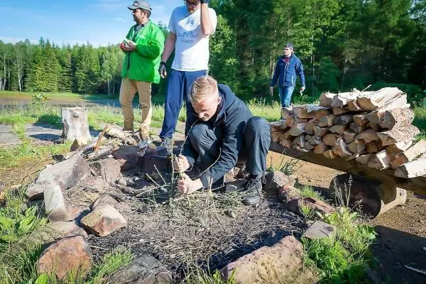 Mann bereitet Zunder im Feuerkreis vor, Holzstapel im Hintergrund