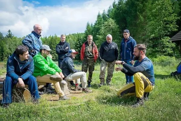 Mann erklärt Technik im Freien, umgeben von Zuhörern auf einer Wiese