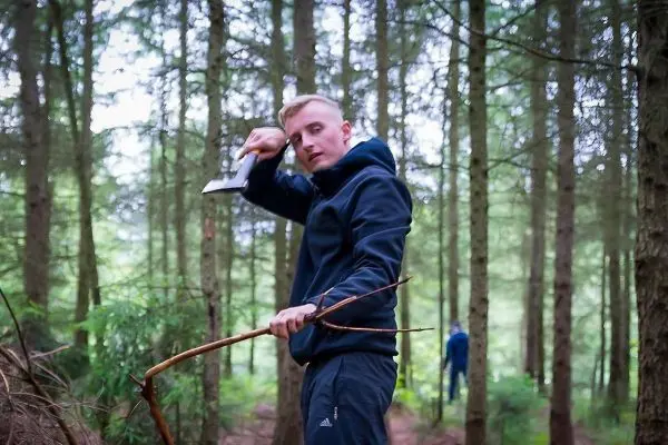 Mann hält Axt und bearbeitet einen Stock im Wald