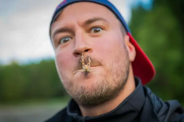 Mann hält eine Heuschrecke vor seinem Gesicht