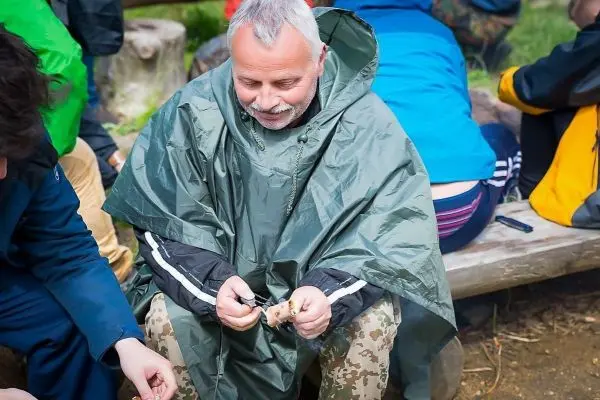 Mann im Poncho bearbeitet Holzstück mit einem Messer
