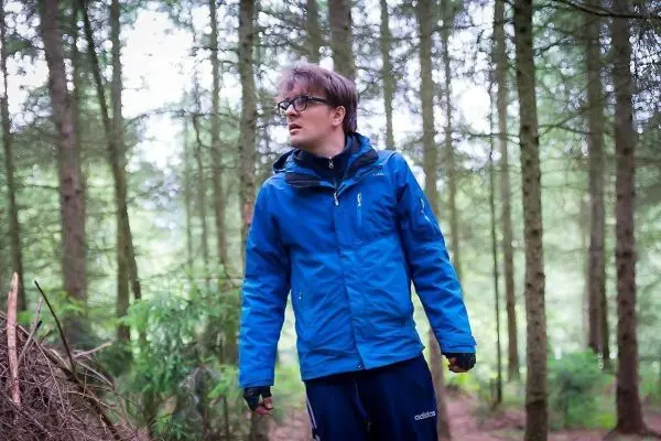 Mann in blauer Jacke steht im Wald und schaut aufmerksam umher