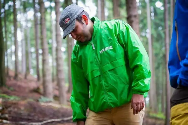 Mann in grüner Jacke beugt sich im Wald über den Boden