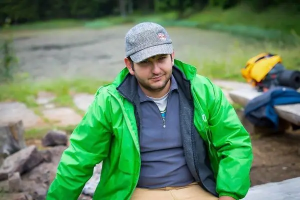 Mann in grüner Jacke sitzt an einem Holzstamm in der Natur