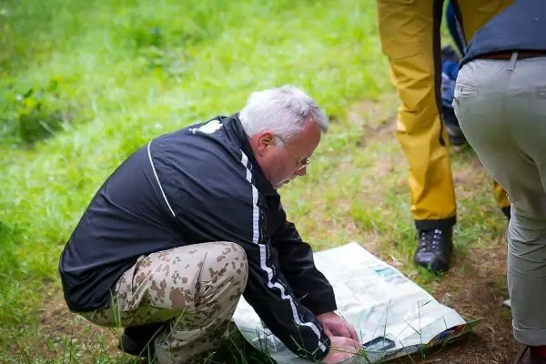 Mann kniet auf dem Boden und studiert eine Karte im Gras