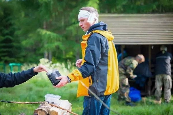 Mann mit Kopfverband nimmt Behälter von einer anderen Person entgegen