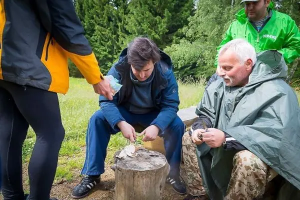 Mann schnitzt mit einem Messer auf einem Baumstamm, während andere zuschauen