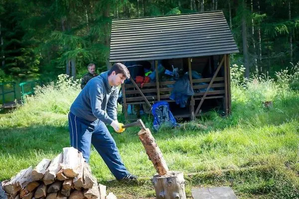 Mann spaltet Holz mit einer Axt neben einem Holzstapel und einer Unterstand