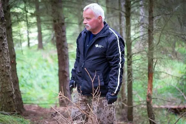 Mann steht in einem Wald zwischen Bäumen und trockenem Gestrüpp