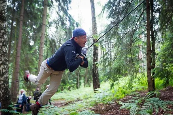 Mann überquert selbstgebaute Seilbrücke zwischen Bäumen im Wald