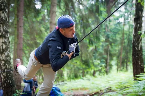 Mann überquert selbstgebaute Seilbrücke zwischen Bäumen im Wald