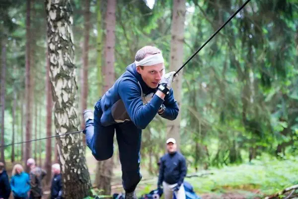 Mann überquert selbstgebaute Seilbrücke zwischen Bäumen im Wald