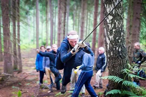 Mann überquert selbstgebaute Seilbrücke zwischen Bäumen im Wald