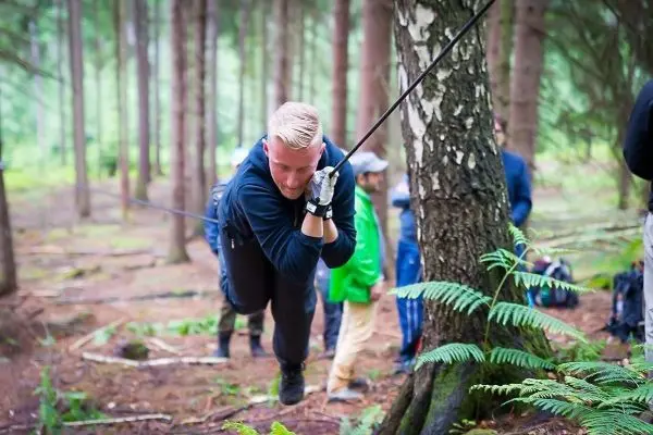 Mann überquert selbstgebaute Seilbrücke zwischen zwei Bäumen im Wald