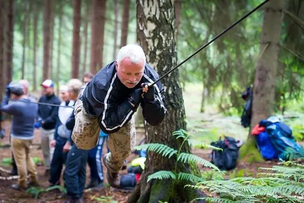 Mann überquert selbstgebaute Seilbrücke zwischen zwei Bäumen im Wald
