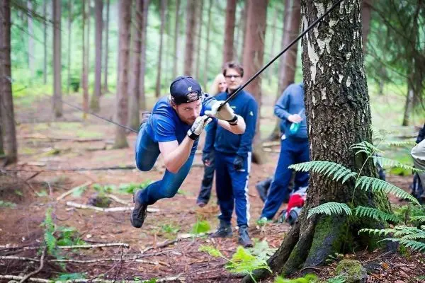 Mann überquert selbstgebaute Seilbrücke zwischen zwei Bäumen im Wald