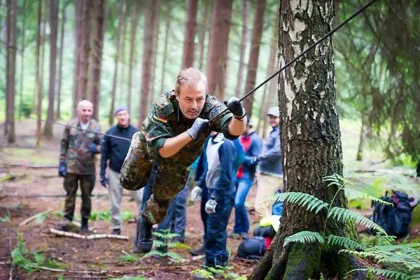 Mann überquert selbstgebaute Seilbrücke zwischen zwei Bäumen im Wald
