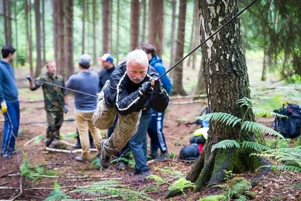 Mann überquert selbstgebaute Seilbrücke zwischen zwei Bäumen im Wald