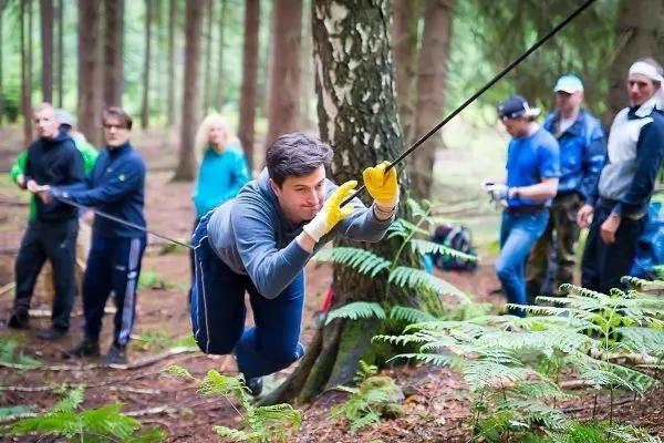 Mann zieht sich an einem Seil entlang eines Baumes durch den Wald