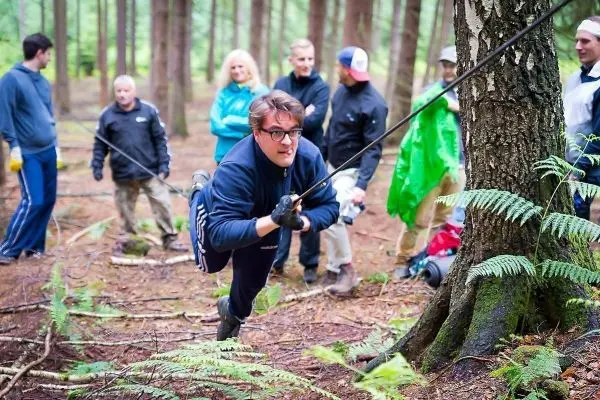 Mann zieht sich an einem Seil zu einem Baum, während andere zuschauen