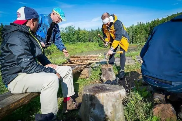 Messer bearbeitet Holz auf einem Baumstumpf, während andere zuschauen