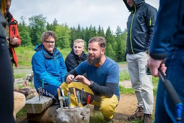 Messer stehen in einem Holzblock, während eine Gruppe um einen Mann sitzt, der erklärt