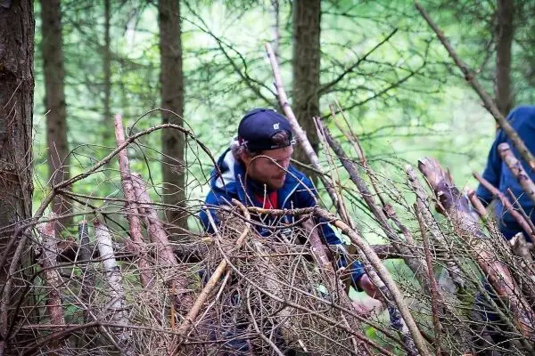 Person baut eine Struktur aus Ästen im Wald