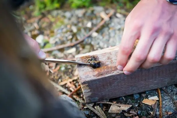 Person bearbeitet Holzstück mit einem Werkzeug beim Überlebenstraining