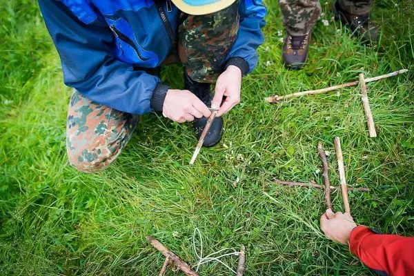 Person formt Äste auf dem Gras beim Überlebenstraining