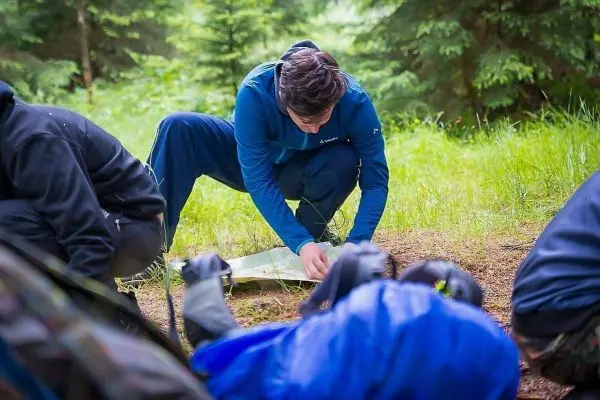 Person kniet auf dem Boden und studiert eine Karte im Wald