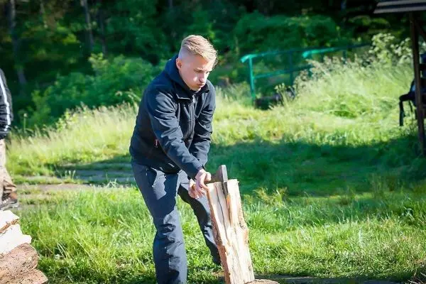 Person spaltet Holz auf einer Wiese beim Überlebenstraining