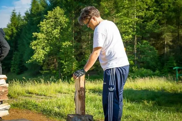 Person steht neben einem Holzblock und bereitet sich auf das Spalten vor