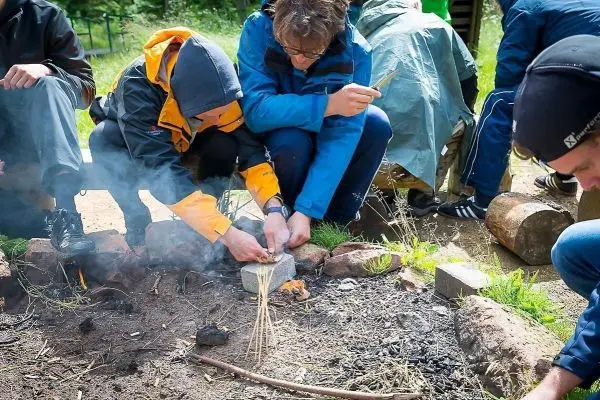 Person zündet Feuerstelle mit Zweigen an beim Überlebenstraining