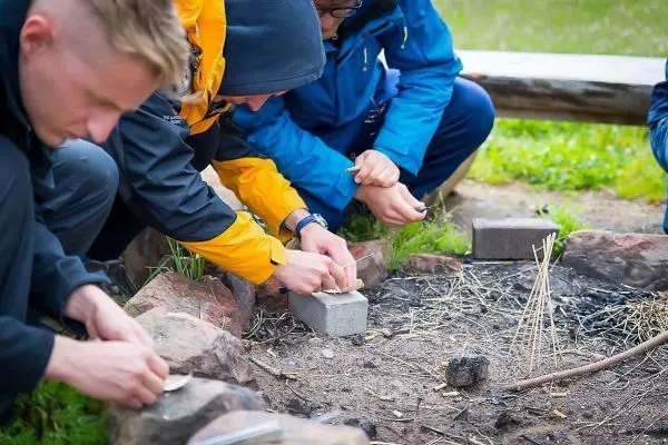 Personen bereiten Feuerstelle mit Steinen und Zündmaterial vor beim Survival Training
