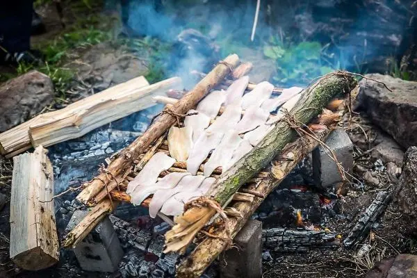 Räucherfisch liegt auf improvisierter Grillkonstruktion über Feuerstelle