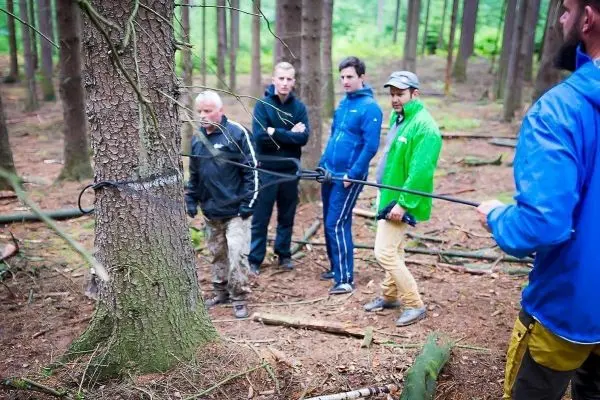 Seilquerung mit einem Seil um einen Baum, mehrere Personen beobachten die Technik