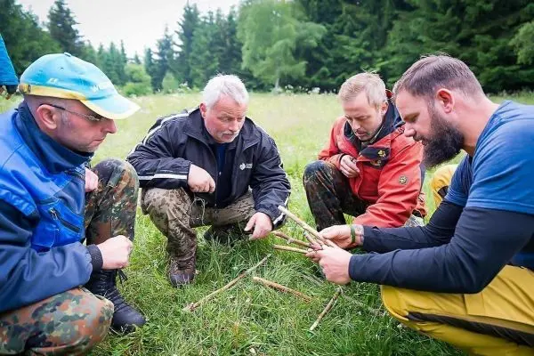 Vier Personen sitzen im Gras und arbeiten mit Holzstöcken