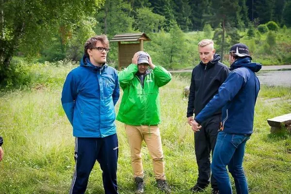 Vier Personen stehen in einer Wiese, eine Person hält sich die Hände am Kopf
